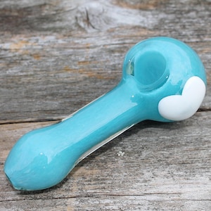 May include: A turquoise glass pipe with a white heart design. The pipe is made of glass and has a smooth, rounded shape.