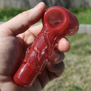 May include: A red glass pipe with a swirling design. The pipe has a bowl and a mouthpiece.