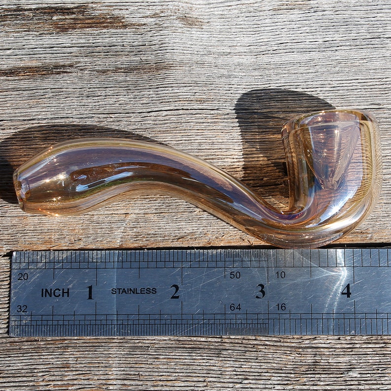 May include: A brown glass pipe with a curved stem and a bowl on the end. The pipe is about 3 inches long and is measured against a ruler.