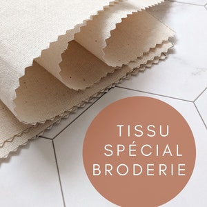 Peut inclure: Gros plan sur une pile de tissu blanc avec un bord en zigzag. Le tissu est étiqueté "TISSU SPECIAL BRODERIE".