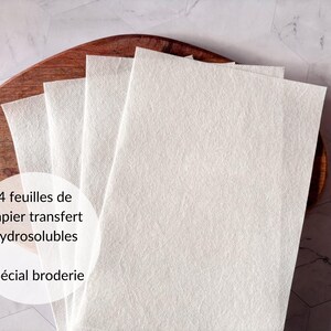 May include: Four sheets of water-soluble transfer paper for embroidery. The paper is white and is stacked on a wooden surface.