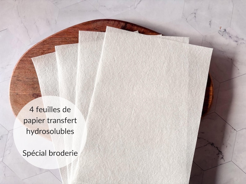 May include: Four sheets of water-soluble transfer paper for embroidery. The paper is white and is stacked on a wooden surface.