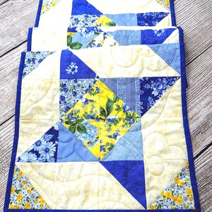Puede incluir: Un camino de mesa acolchado con un patr&oacute;n floral azul y amarillo. El camino de mesa est&aacute; hecho de cuadrados de tela cosidos juntos en un patr&oacute;n geom&eacute;trico. El camino de mesa tiene un borde azul y est&aacute; acolchado con un patr&oacute;n ondulado. El texto "Style #1" es visible en la imagen.