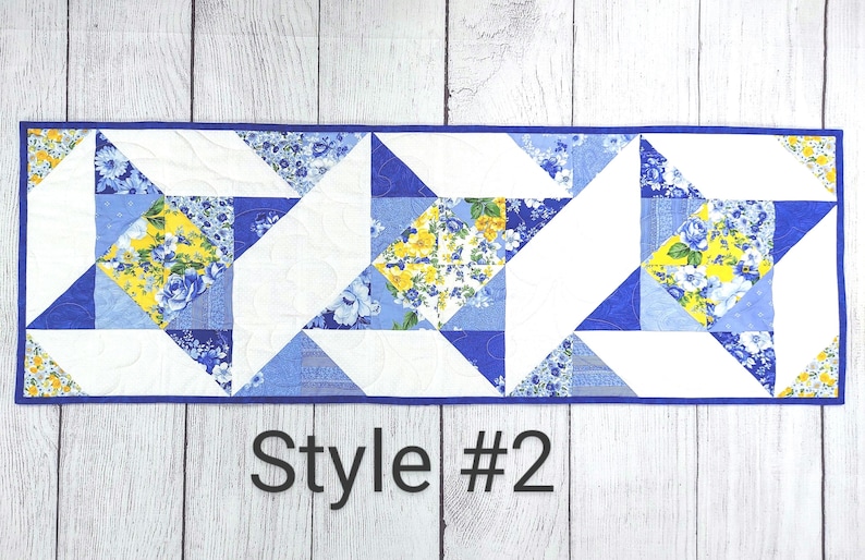 Puede incluir: Un camino de mesa azul y amarillo con un patr&oacute;n geom&eacute;trico. El camino de mesa est&aacute; hecho de tela y tiene un fondo blanco con tri&aacute;ngulos de estampado floral azul y amarillo. El texto "Style #2" est&aacute; impreso debajo del camino de mesa.