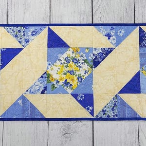 Puede incluir: Un camino de mesa acolchado azul y amarillo con un patr&oacute;n geom&eacute;trico. El camino de mesa est&aacute; hecho de tela con estampado floral.