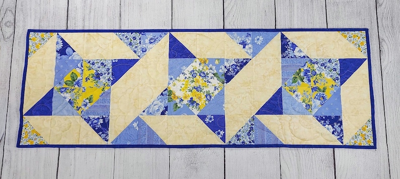 Puede incluir: Un camino de mesa acolchado azul y amarillo con un patr&oacute;n geom&eacute;trico. El camino de mesa est&aacute; hecho de tela con estampado floral.