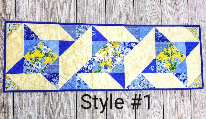 Puede incluir: Un camino de mesa acolchado azul y amarillo con un patr&oacute;n geom&eacute;trico. El camino de mesa est&aacute; hecho de recortes de tela y tiene un borde azul. El texto "Style #1" est&aacute; impreso debajo del camino de mesa.