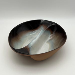 May include: A divided ceramic serving dish with a brown, white, and black glaze. The dish has a unique, organic shape.