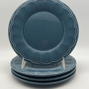 May include: Four teal ceramic plates with a scalloped edge are stacked, with one plate upright. The plates have a glossy finish. The plates are displayed against a white background. The plates are suitable for serving food.