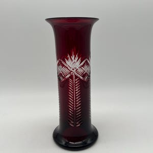 May include: A ruby red glass vase with a flared top and a round base. The vase features a detailed, etched design of a floral pattern. The vase is approximately 10 inches tall.