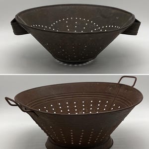 Op de afbeelding: Twee vintage metalen vergietjes met handvatten. Beide vergietjes zijn roestig en hebben een bruine patina. De vergietjes hebben een ronde vorm met een brede basis en een smalle bovenkant. De vergietjes hebben gaten over de hele bodem.