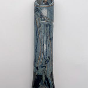 May include: A tall, cylindrical ceramic wall vase with a glossy blue and dark navy glaze. The surface features vertical, textured drip patterns and a small hole at the top for hanging, threaded with a thin, natural-colored twine string.