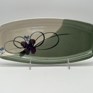 May include: An oval ceramic serving tray with a green and beige glaze. The tray features a black floral design with purple and blue accents.