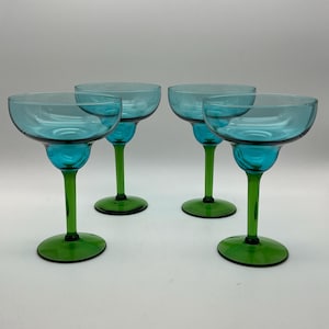 Könnte beinhalten: Vier Margarita-Gläser mit türkisfarbenen Schalen und grünen Stielen und Böden. Die Gläser haben ein klassisches Design, ideal zum Servieren von Cocktails. Die Stiele sind lang und schlank, und die Böden sind rund.