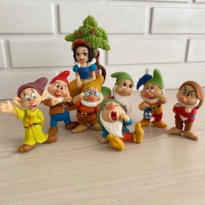 Può includere: Set di figurine di Biancaneve e i Sette Nani. Il set include Biancaneve seduta su un ceppo d'albero e sette nani in diverse pose. I nani sono fatti di pasta di zucchero e sono dipinti con colori vivaci.