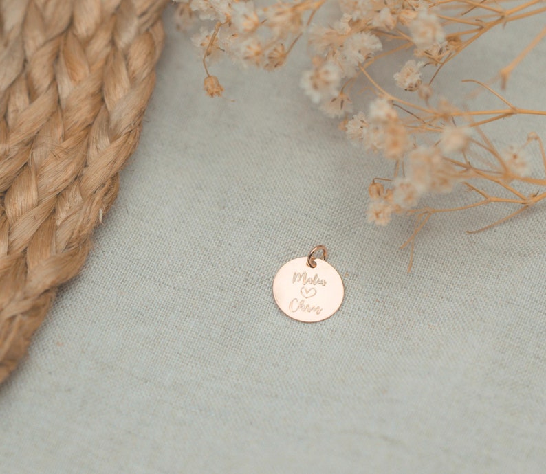 May include: A gold-toned round charm with the words "Mela & Chris" engraved on it, with a small heart symbol between the names.