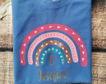 May include: A blue t-shirt featuring a rainbow design and the text "6 Josephine" in gold.