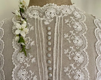 May include: White lace top with a high neckline and a row of buttons down the back. The lace is delicate and intricate, with a floral pattern. The top is perfect for a special occasion.