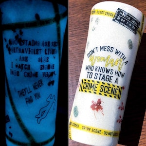 May include: A white glitter tumbler featuring yellow crime scene tape, a black police department stamp, red blood splatter, and fingerprints. The text reads: Don't mess with a woman who knows how to stage a crime scene. The design glows in the dark.