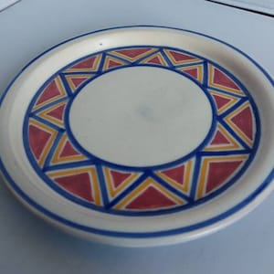 Puede incluir: Un plato de cerámica blanco con un patrón geométrico azul, amarillo y rojo alrededor del borde.