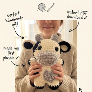 Peut inclure: Une peluche de vache au crochet faite &agrave; la main, de couleur cr&egrave;me, grise et noire, tenue par une personne. L'image comprend le texte : &laquo; Je n'aurais jamais cru que je pourrais crocheter &raquo;. Le texte indique &eacute;galement un patron pour d&eacute;butants, un cadeau parfait et r&eacute;alisable en un week-end.
