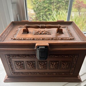 May include: A wooden box with intricate carvings and a decorative metal latch. The box has a brown finish and a carved wooden handle.