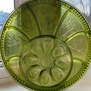 Op de afbeelding: Een groene glazen serveerschaal met zes afzonderlijke secties en een middelste sectie met zes inkepingen. De schaal heeft een decoratief geëtst ontwerp van bladeren en takken.