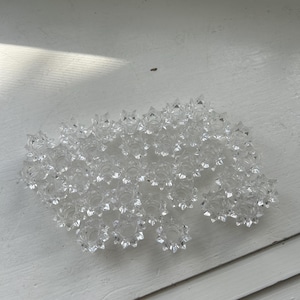 May include: A large group of clear crystal chandelier prisms, arranged in a circular pattern. The prisms are faceted and have a starburst design.