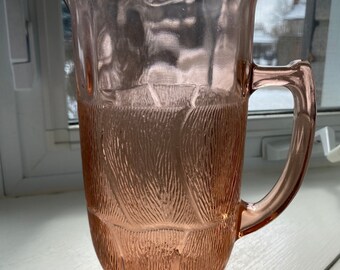 May include: A pink glass pitcher with a textured design. The pitcher has a wide mouth and a handle.