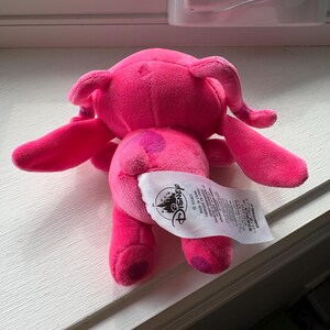 May include: A plush pink Angel doll, featuring large ears, long arms, and a tail. The doll has a Disney tag attached. The plush toy is made of soft material and is designed to resemble the character Angel.