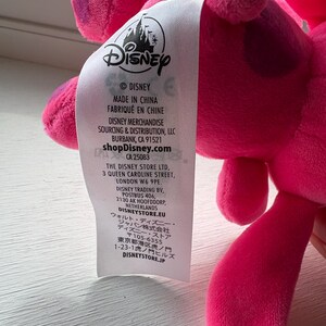 May include: A pink plush toy with a Disney label attached. The label includes the Disney logo, the text "MADE IN CHINA", and the shopDisney.com website address. The toy is a vibrant pink color.
