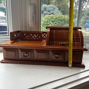 May include: A vintage wooden jewelry box with a roll-top design and four drawers. The box is approximately 9 inches tall. The drawers have metal pulls. The box is made of dark brown wood and sits on a white surface.