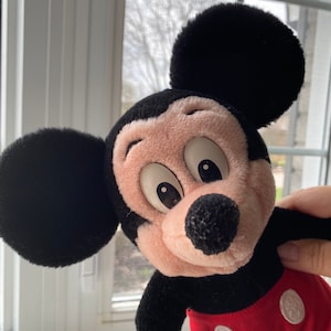 May include: A plush Mickey Mouse toy with black ears, a black body, a pink face, and red shorts with white circles.
