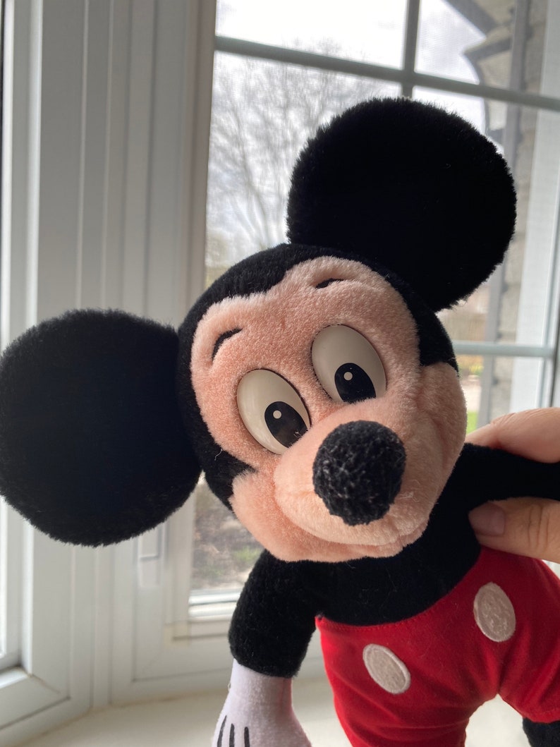 May include: A plush Mickey Mouse toy with black ears, a black body, a pink face, and red shorts with white circles.