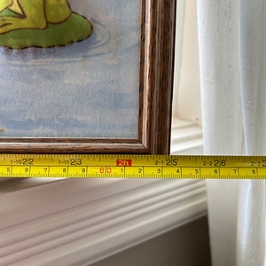 May include: A framed picture of a green frog on a blue background. The picture is 2 feet wide and is measured with a yellow tape measure.
