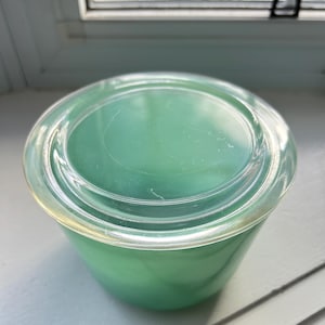 May include: A vintage green glass storage container with a clear glass lid. The container is round and has a smooth, glossy finish.