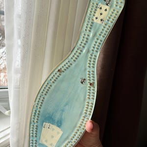 Op de afbeelding: Een transparante plastic bowlingpin met een blauw en wit marmerpatroon. De pin heeft een nummerschaal aan de zijkant en een scorekaart voor een kaartspel aan de voorkant. De scorekaart toont een vijf van schoppen en een vijf van harten.