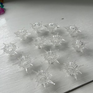 May include: Twelve clear plastic star-shaped candle holders with a raised centre for a candle.