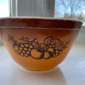 May include: A brown and white mixing bowl with a black and white design of grapes and apples. The bowl is made of ceramic and has a vintage look.