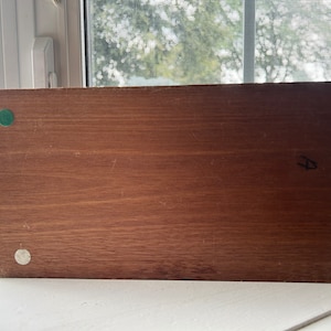 May include: A rectangular wooden object with a dark brown finish. The object has four small, circular pads on the corners. The pads are green and white. The object is sitting on a white surface.