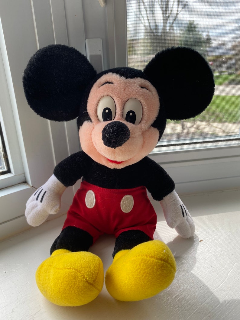 May include: A plush Mickey Mouse toy with black ears, a black body, red shorts with two white buttons, and yellow shoes.