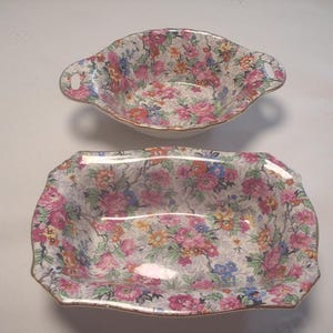 Peut inclure: Deux plats de service à motifs floraux. Le plat supérieur est un petit bol avec des poignées. Le plat inférieur est rectangulaire. Les deux plats ont un fond blanc avec des fleurs roses, bleues et jaunes.