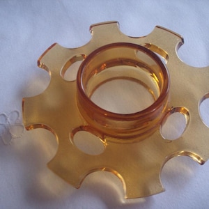 May include: Amber glass candle holder with a starburst design and eight open slots. The holder has a central ring for a candle.
