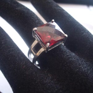 May include: A silver ring with a large, square, red gemstone.