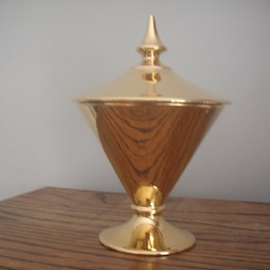 May include: A gold-coloured ceramic candy dish with a pointed lid. The dish is shaped like a cone and has a wide base.