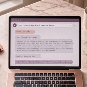 May include: A rose gold laptop displaying a digital task management interface with text including Draft a follow-up email after a stakeholder meeting, Owner: John Smith, Task: Prepare project update, and Deadline: August 18, 2024, on a marble surface.