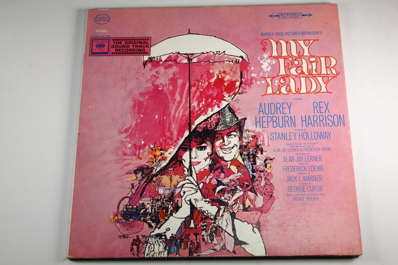 May include: A pink and white vinyl record cover for the musical "My Fair Lady" featuring Audrey Hepburn and Rex Harrison. The cover art depicts a scene from the musical with a large umbrella and a crowd of people.