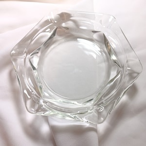 Può includere: Un posacenere in vetro trasparente con forma esagonale e un bordo leggermente rialzato.