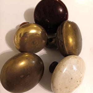May include: Four vintage door knobs, two are brass, one is brown ceramic, and one is white ceramic.