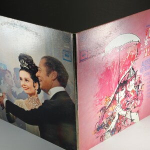 May include: A vintage vinyl record album cover for the musical "My Fair Lady" starring Audrey Hepburn and Rex Harrison. The front cover features a colorful illustration of the characters in a scene from the musical. The back cover features a photo of Audrey Hepburn and Rex Harrison dancing.